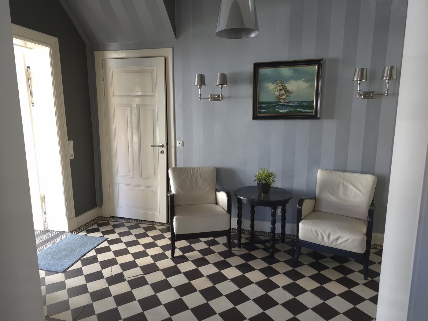 Eingangsbereich mit zwei Sesseln, Tisch und Wandbild an gestreifter Wand.