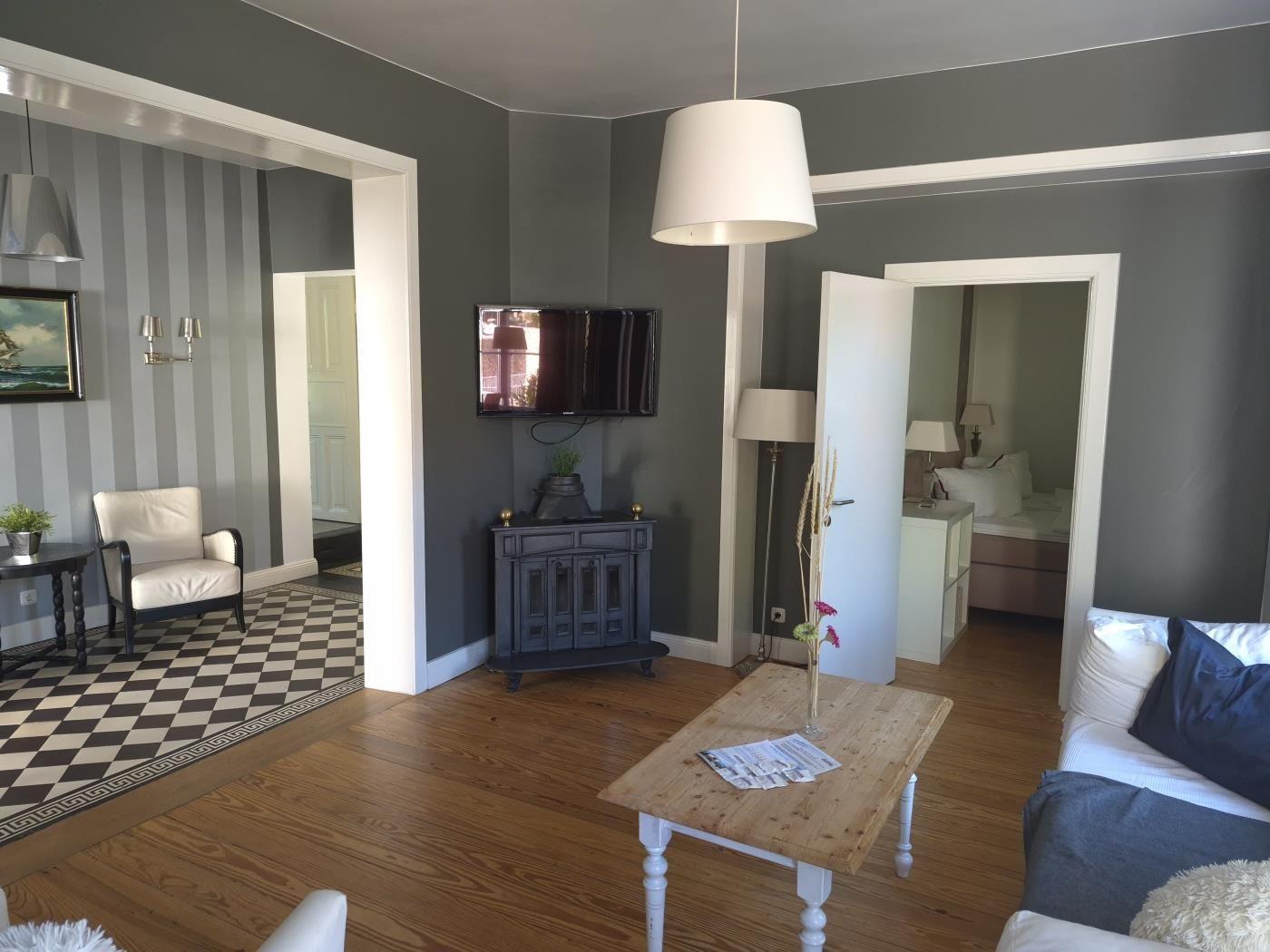 Wohnzimmer mit Sofa, Holztisch und Fernseher. Durchgänge zu Schlafzimmer und Wohnbereich mit Streifenwand.