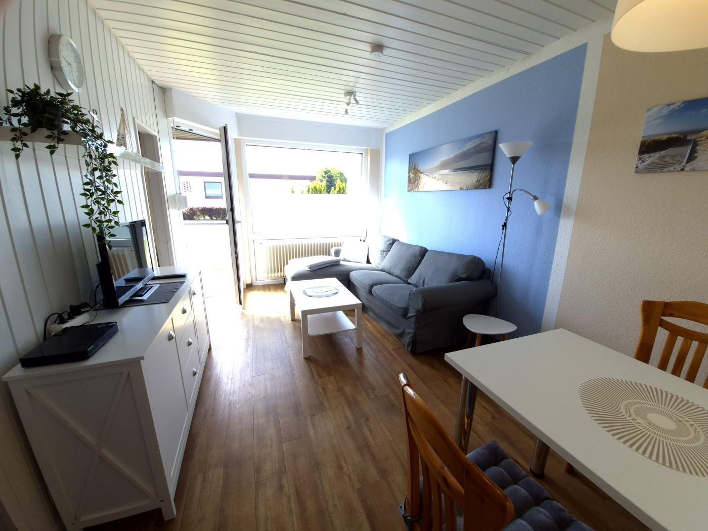 Wohn- und Essbereich mit Sofa, Tisch und TV. Holzfußboden und blaue Wand.