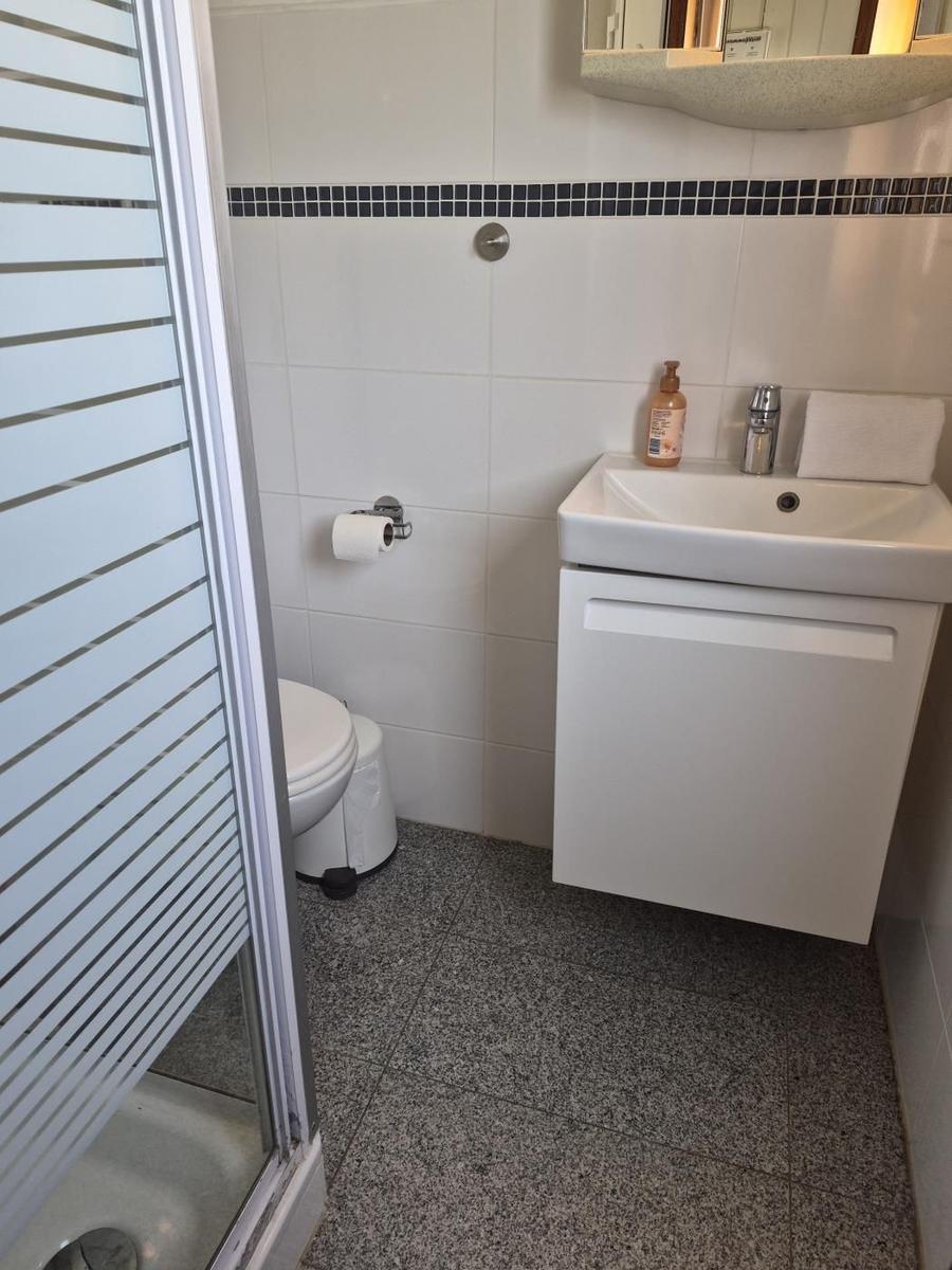 Badezimmer mit Waschbecken, Toilette und Dusche. Weiße Fliesen und grauer Boden.