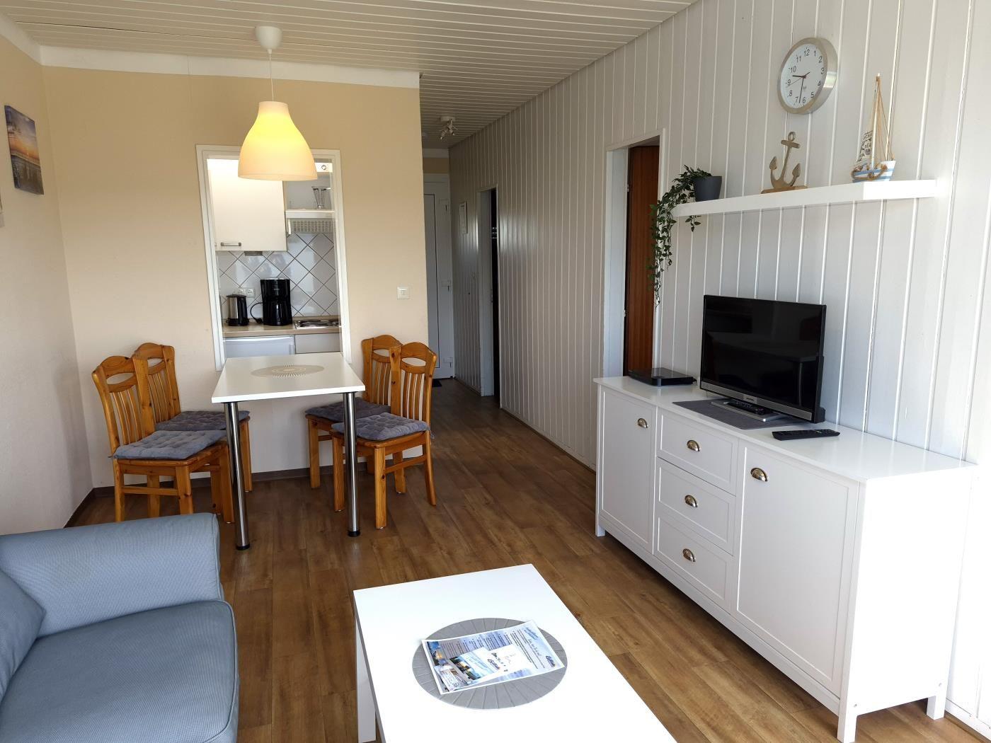 Wohn- und Essbereich mit Küchenzeile, TV und Holzboden.