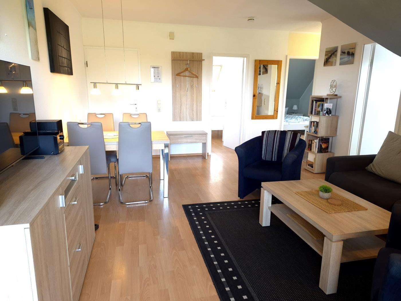 Wohn- und Essbereich mit Holzboden, Sofa, Sessel und Esstisch mit Stühlen.