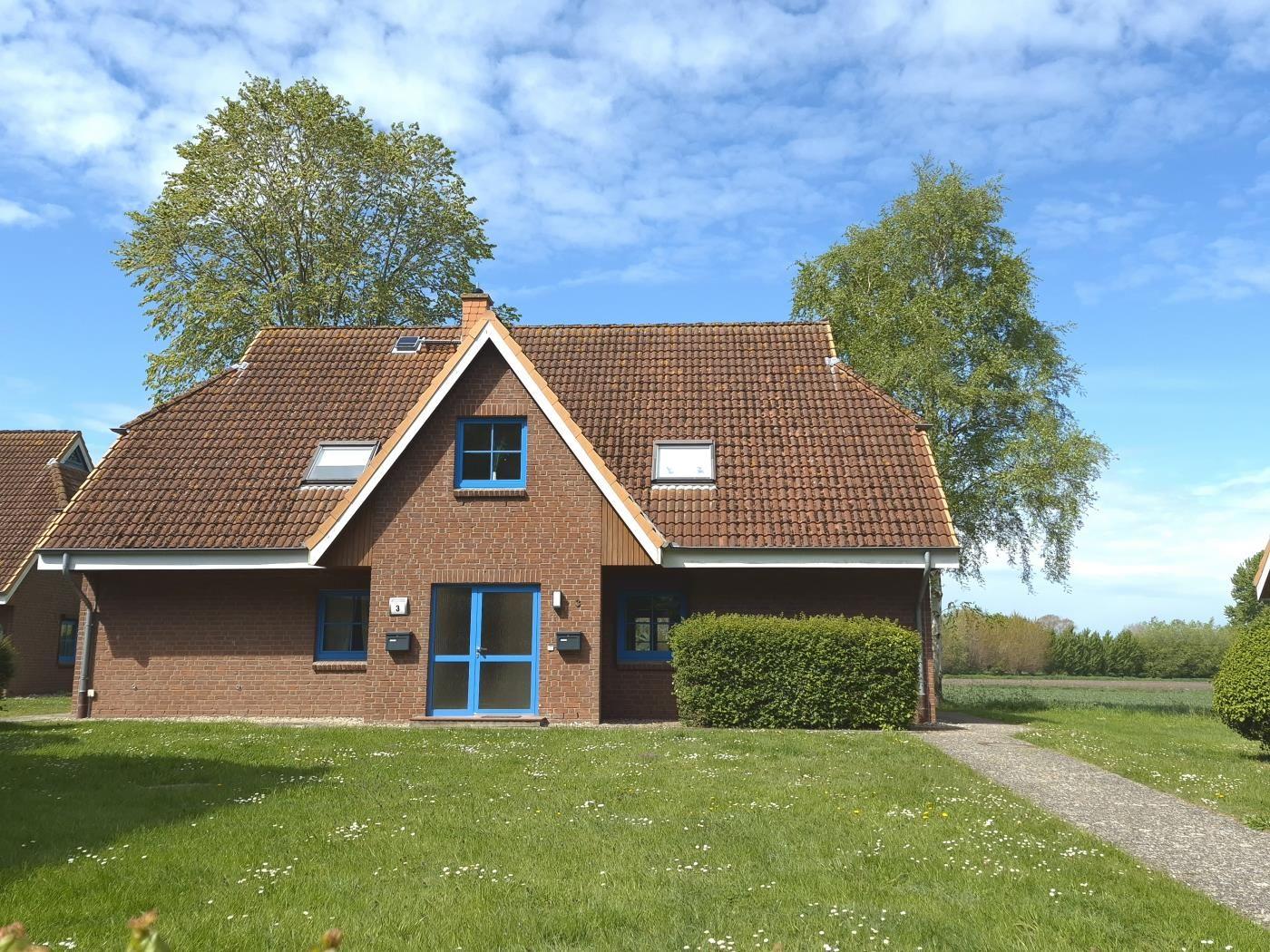 Ein zweistöckiges Haus mit rotem Dach und blauer Tür steht auf einer grünen Wiese.