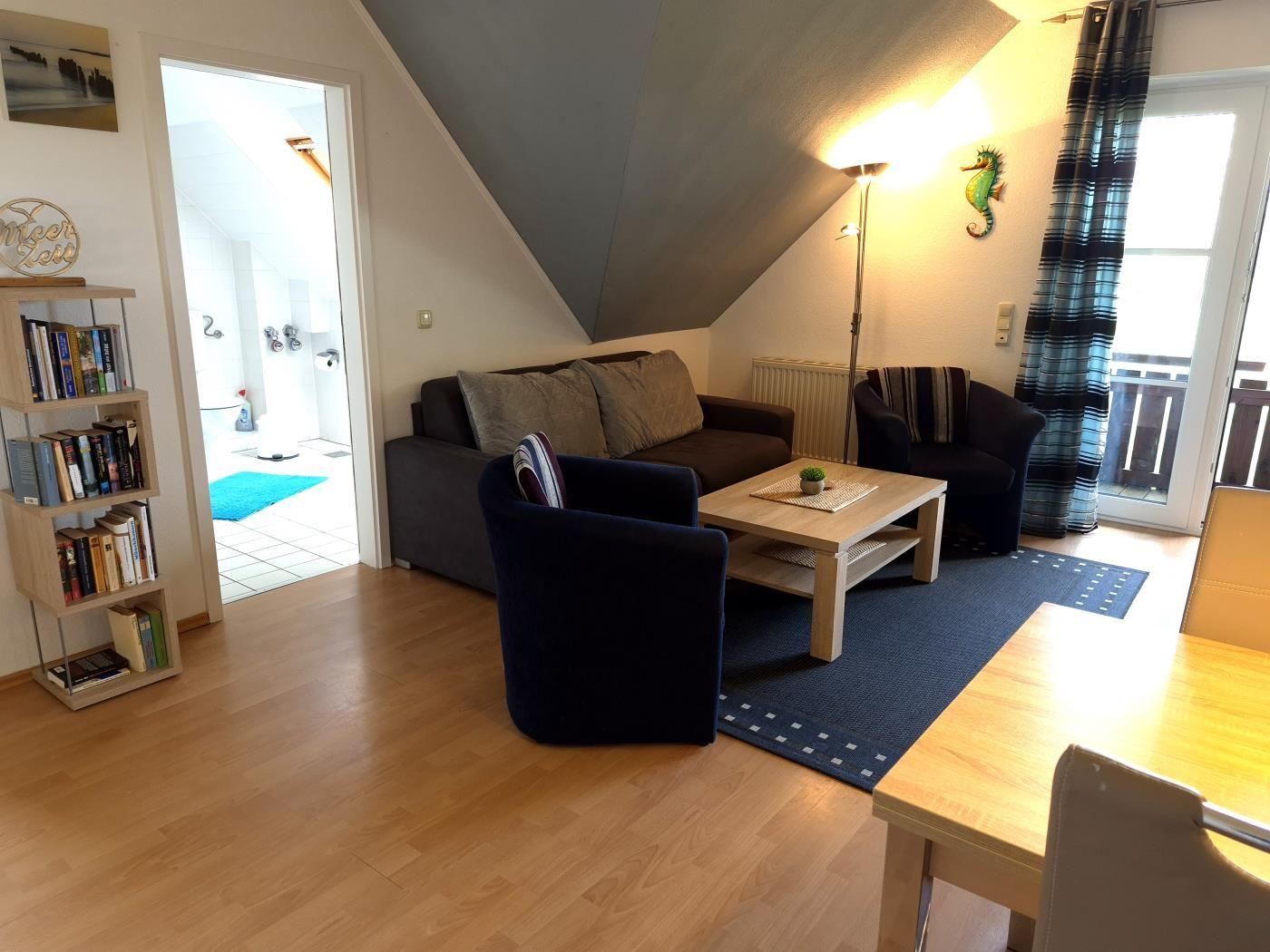 Wohnbereich mit Sofa, Sessel und Tisch. Durchgang zur Badewanne. Balkon mit Vorhang.