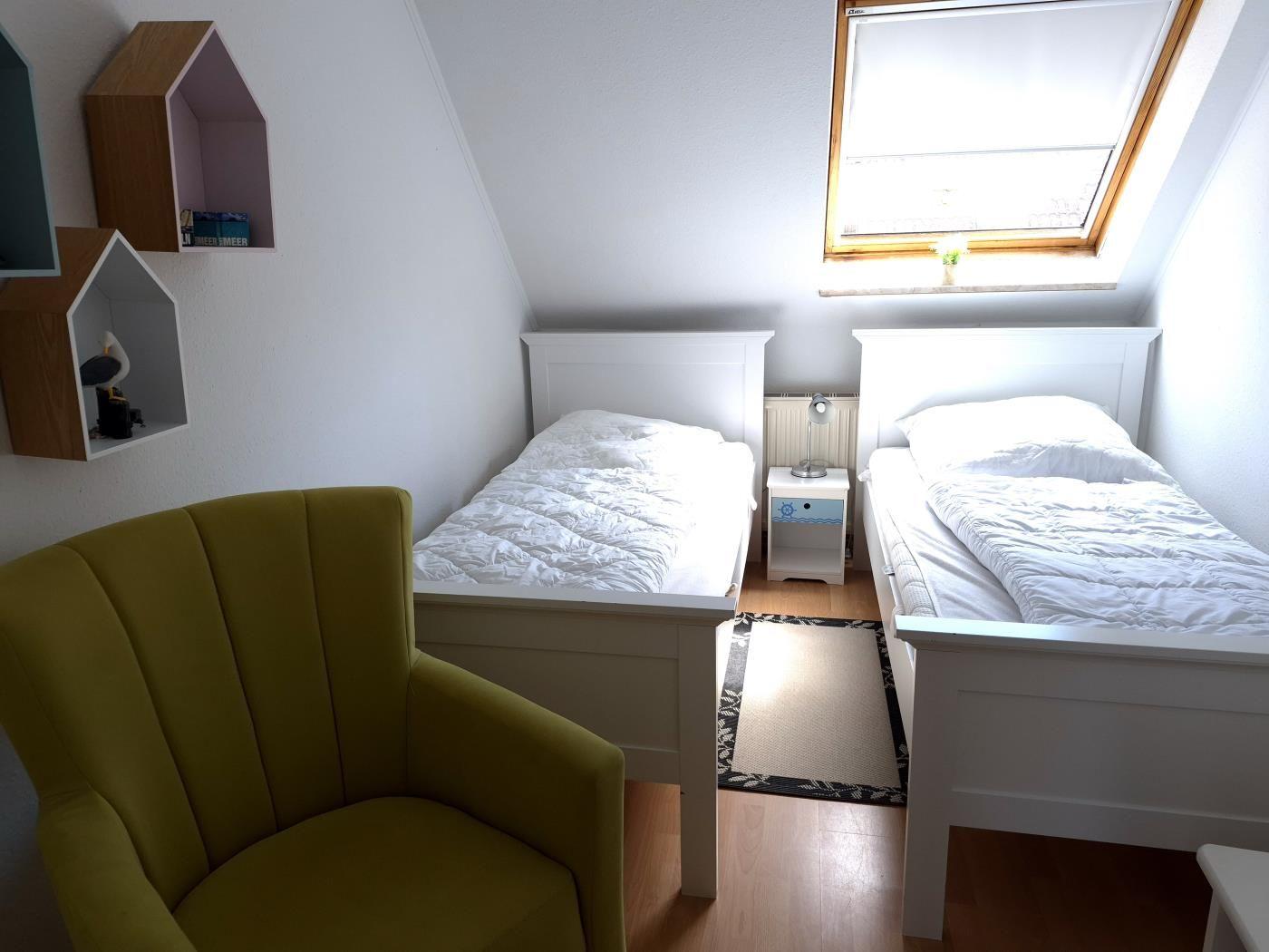 Zwei Einzelbetten, ein gelber Sessel und ein Dachfenster.