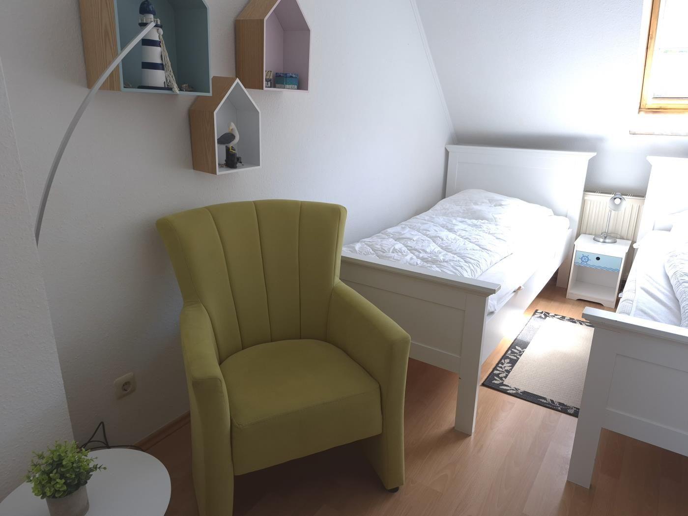 Ein Zimmer mit zwei Betten, einem gelben Sessel und einem Nachttisch.