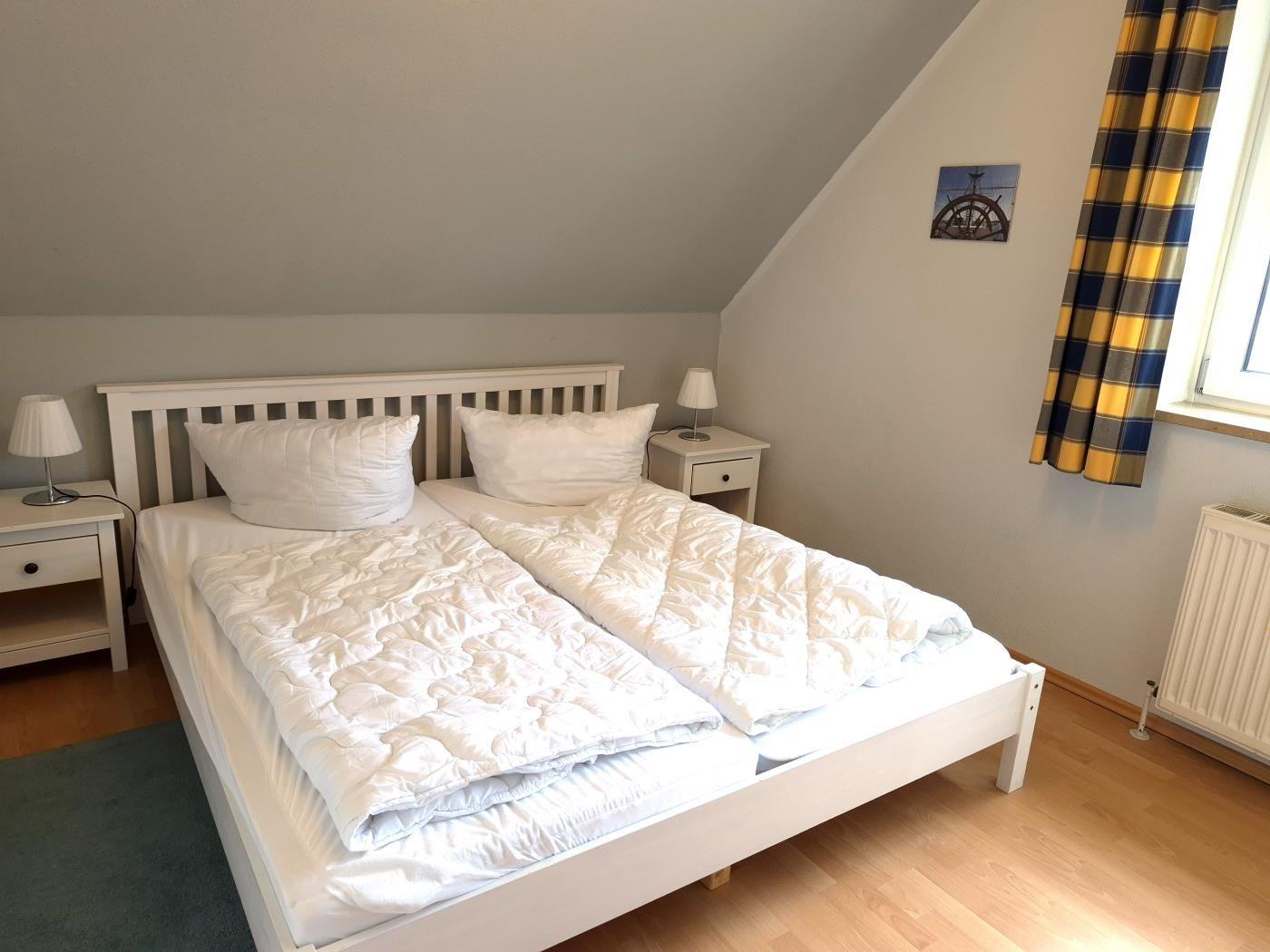 Schlafzimmer mit Doppelbett, zwei Nachttischen und Fenster mit gelb-blauen Vorhängen.