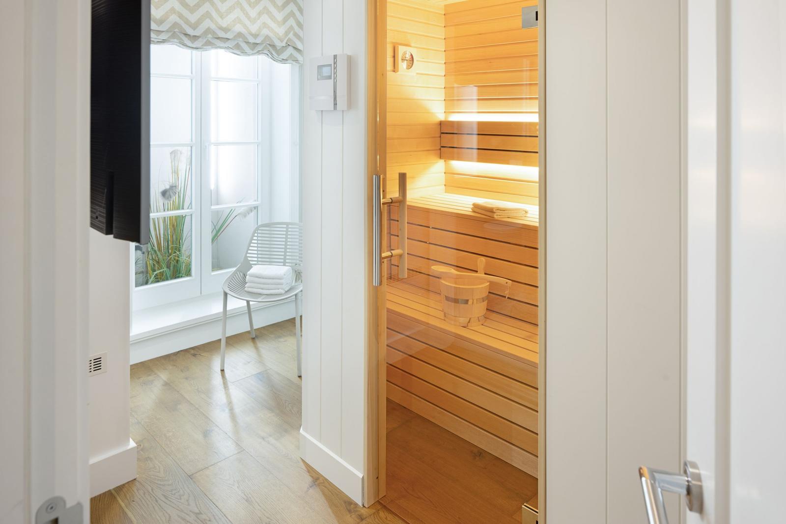 Sauna mit Holzbank und Eimer. Nebenraum mit Fenster und Stuhl.