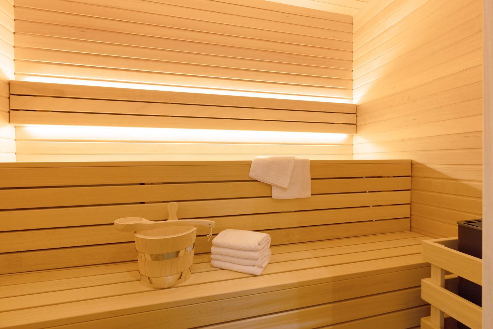 Sauna mit Holzbank, Handtuch und Eimer. Warm beleuchtete Holzwände.