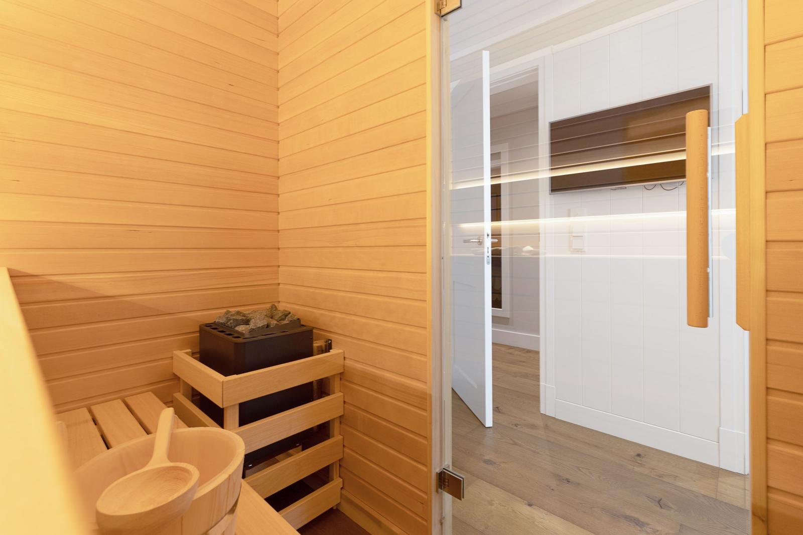 Sauna mit Holzwand und Holzbank. Tür führt in einen Flur mit weißer Wand.