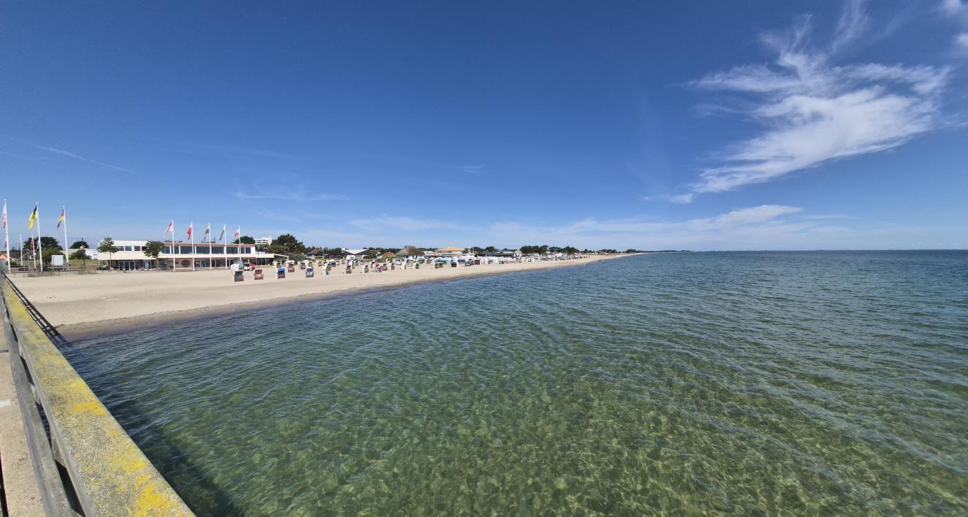 Strand mit klarem Wasser und Strandkörben unter blauem Himmel.