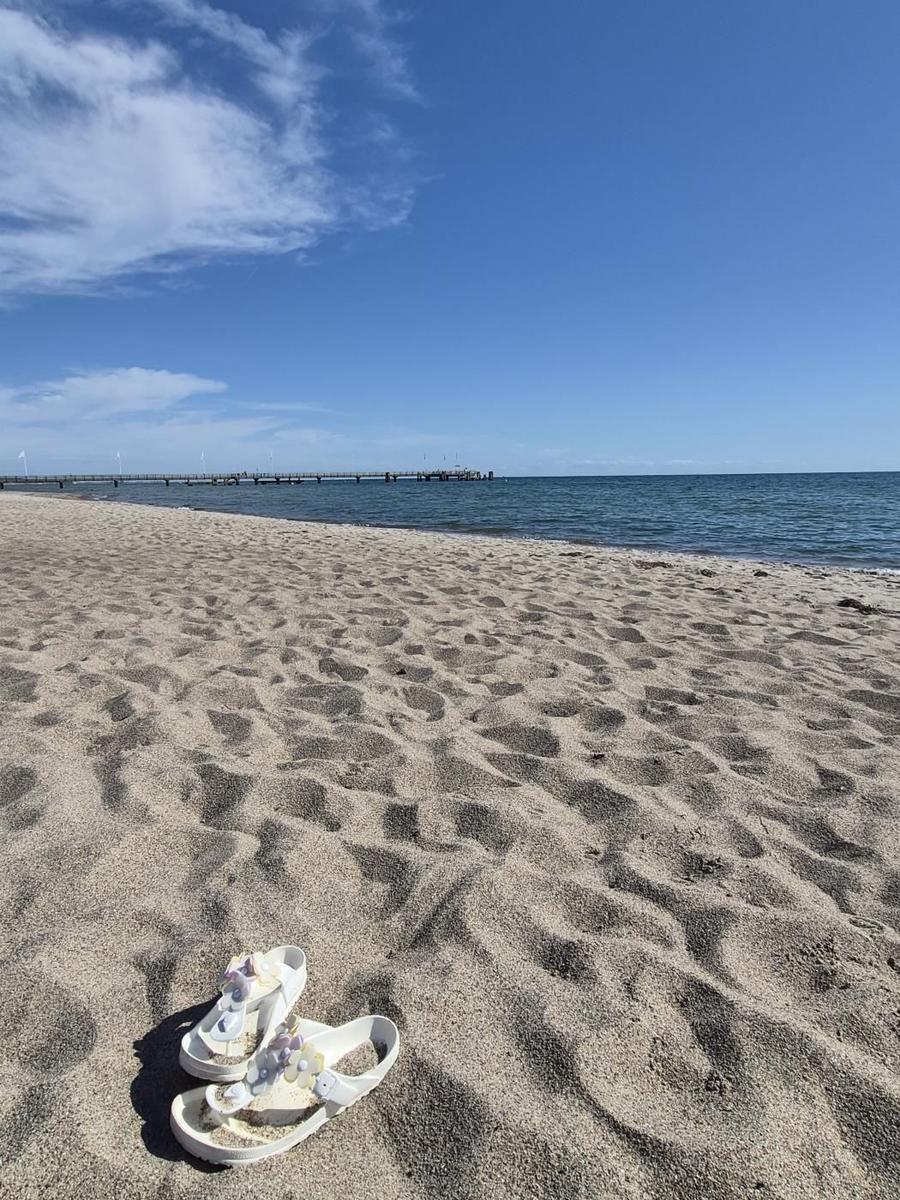 Weiße Sandalen liegen am Strand, im Hintergrund See und Pier.