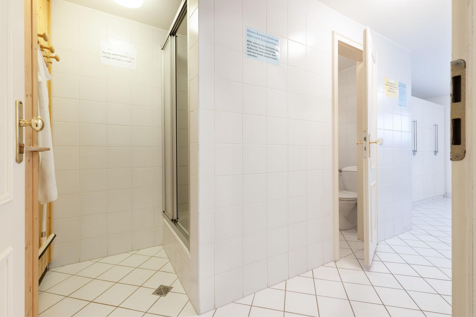 Dusche, Toilette und Duschbereich mit weißen Fliesen und Türöffnungen.