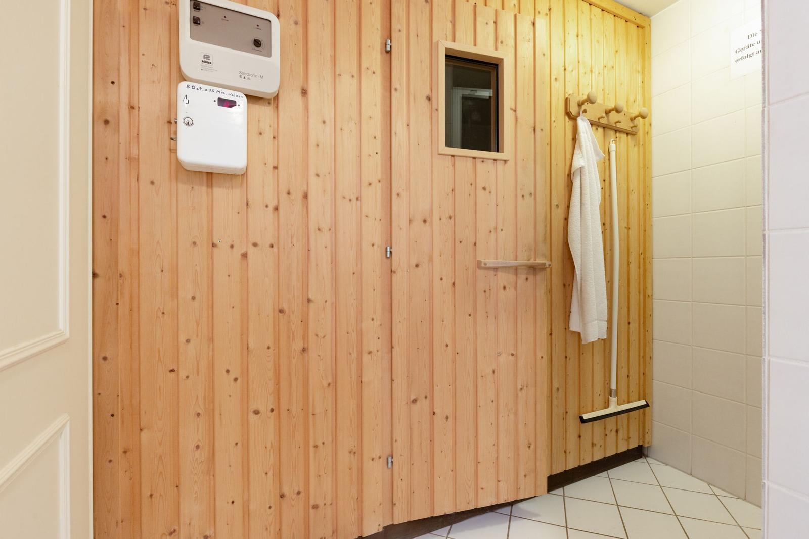 Sauna mit Holzwand, Steuerung und Handtuchhalter. Fliesenboden und Fenster.