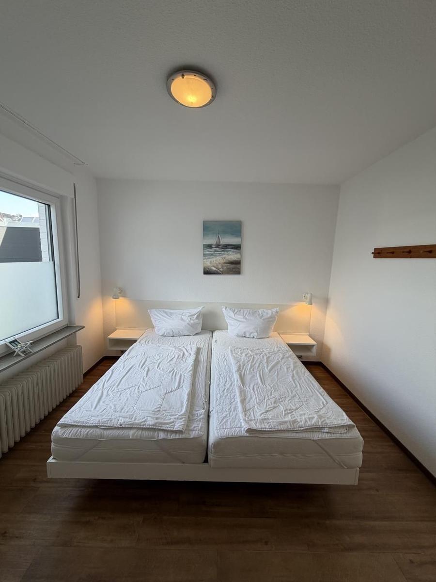 Schlafzimmer mit Doppelbett, Fenster und Wandbild. Holzboden und Deckenleuchte.