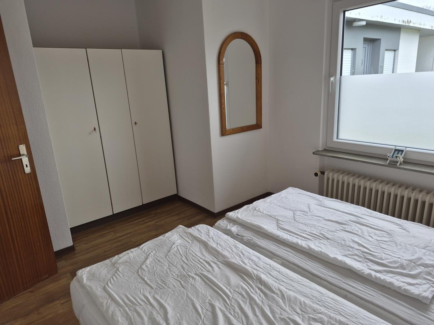 Zwei Betten, Kleiderschrank, Spiegel und Fenster mit Heizkörper.