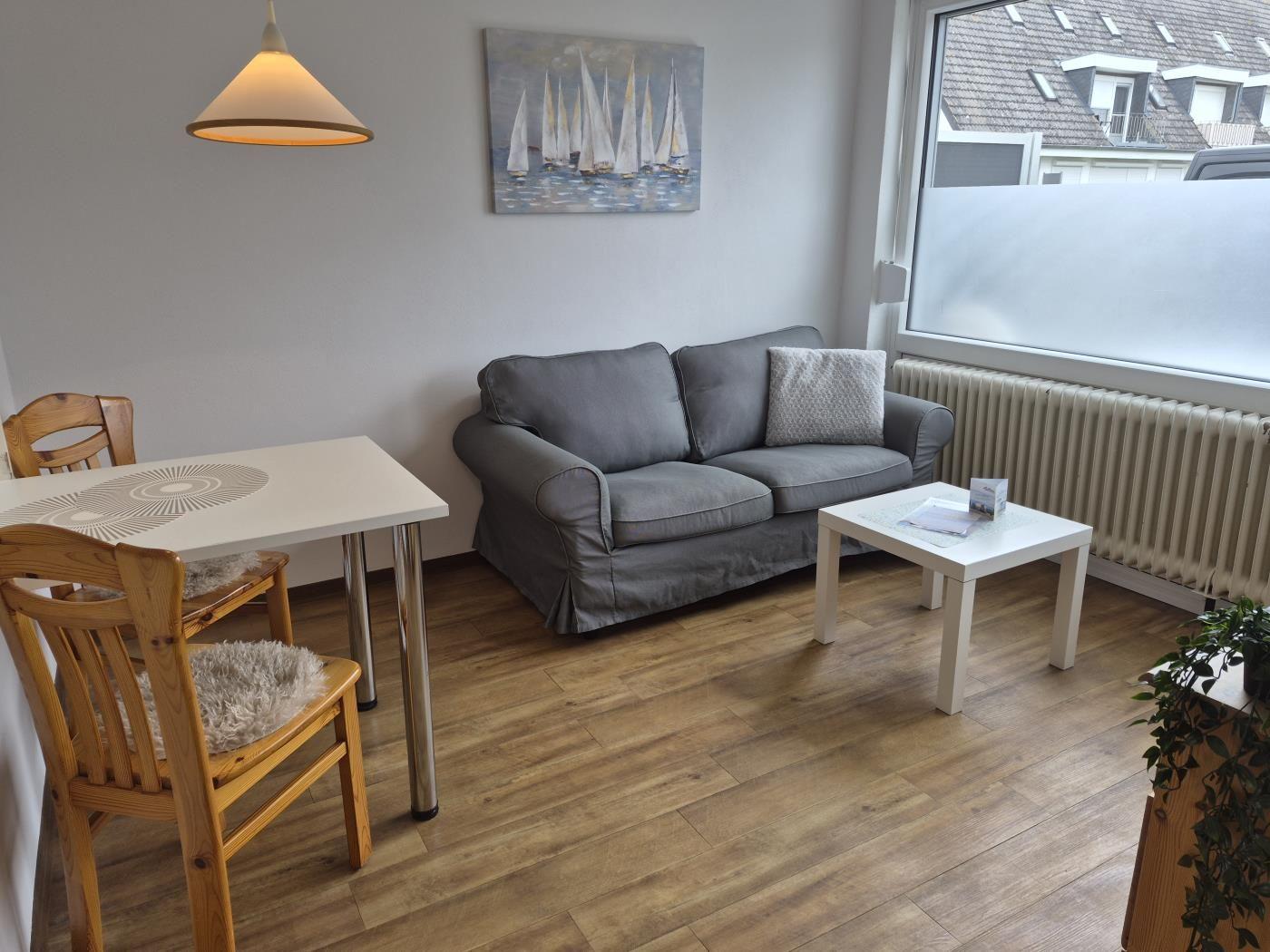 Wohnzimmer mit Sofa, Tisch und Stühlen. Wandbild mit Segelbooten und großes Fenster.