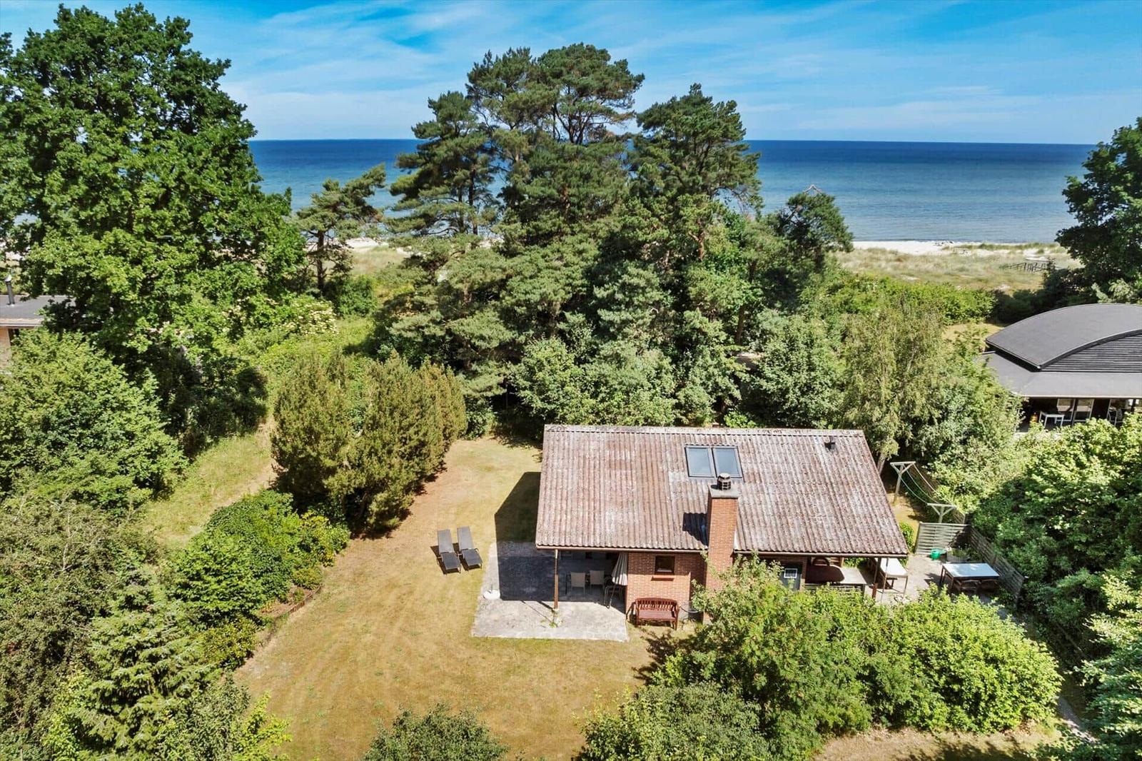 Haus mit Terrasse und Garten, umgeben von Bäumen, mit Blick auf das Meer.