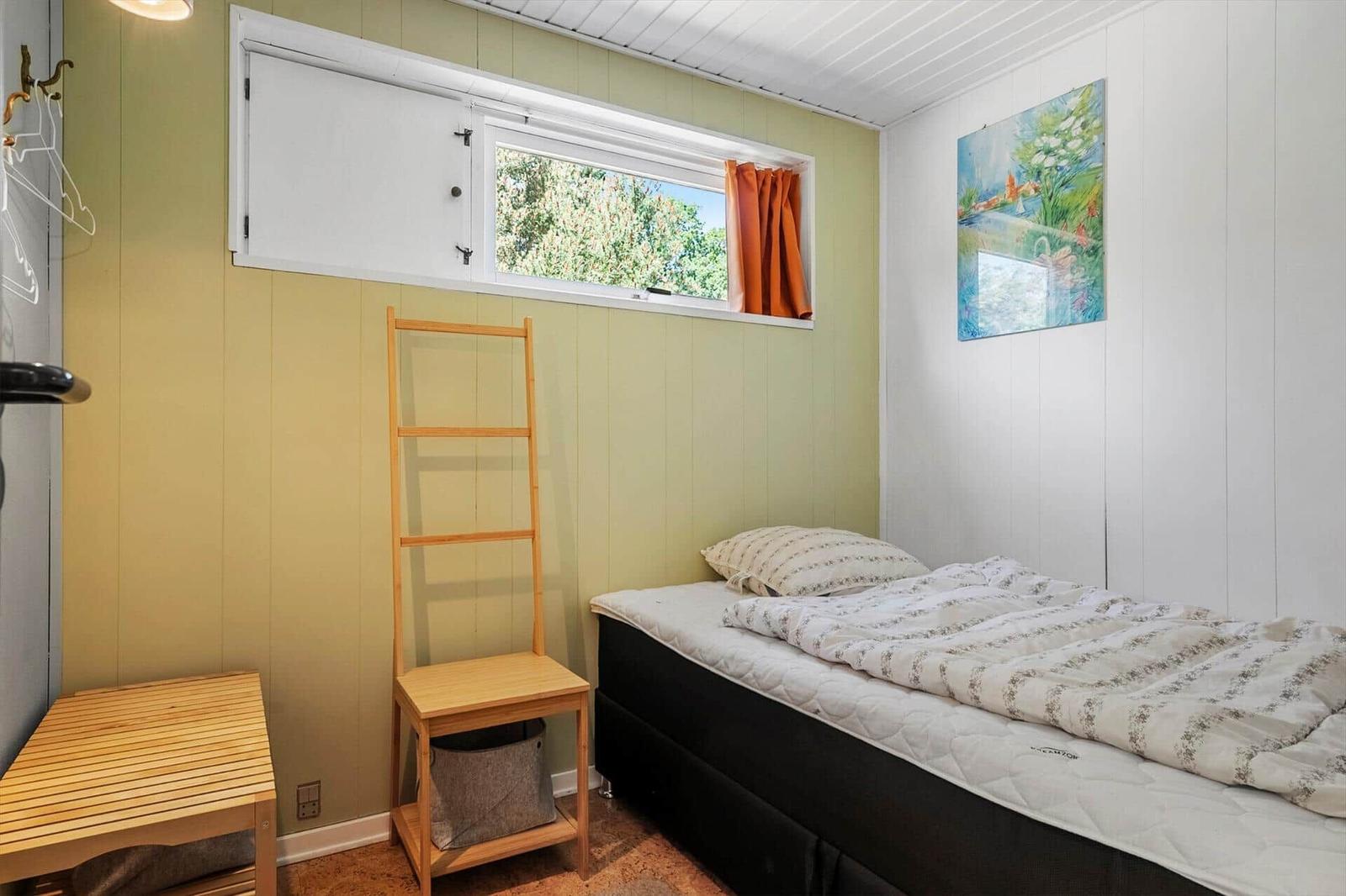 Ein Schlafzimmer mit Bett, Holzregal und Fenster. Wandfarbe cremeweiß und hellgrün.