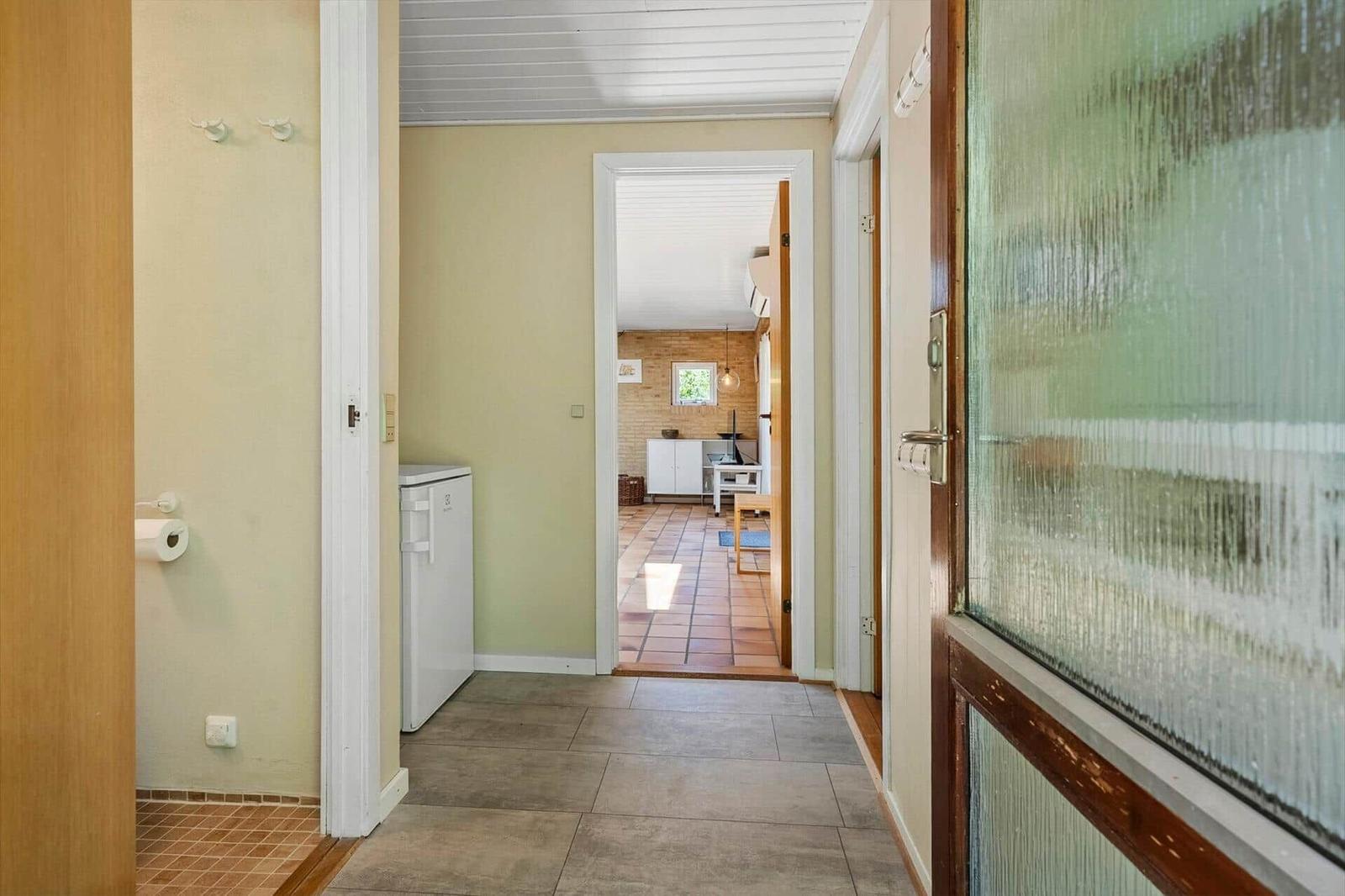 Flur mit Kühlschrank und Blick in Küche mit Terrakottboden und Backsteinwand.
