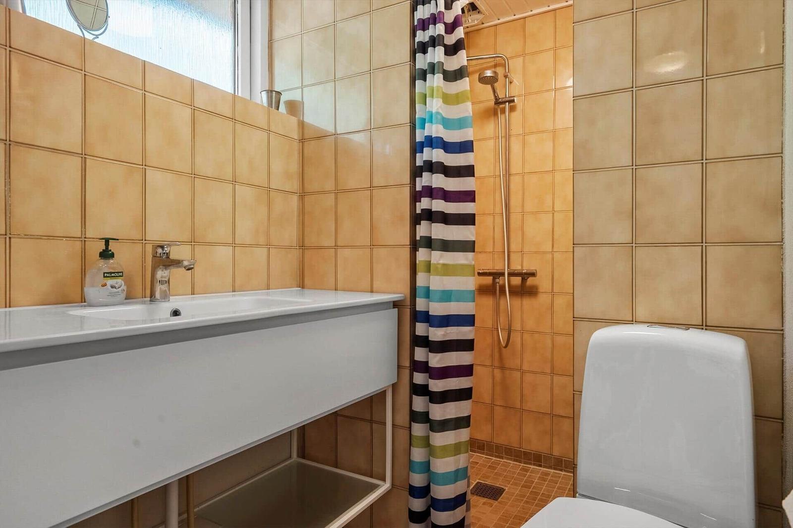 Badezimmer mit Waschbecken, Dusche und Toilette. Wandfliesen und buntes Duschvorhang.