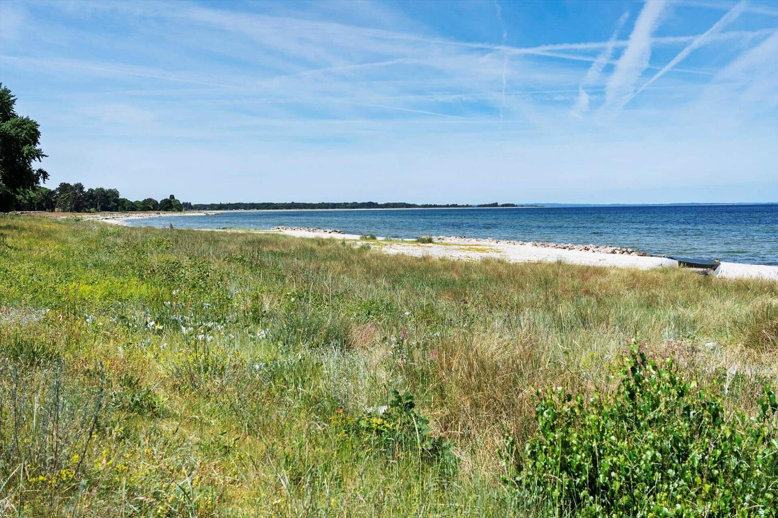 Weitläufiger Strand mit Grasland und blauem Meer unter klarem Himmel.