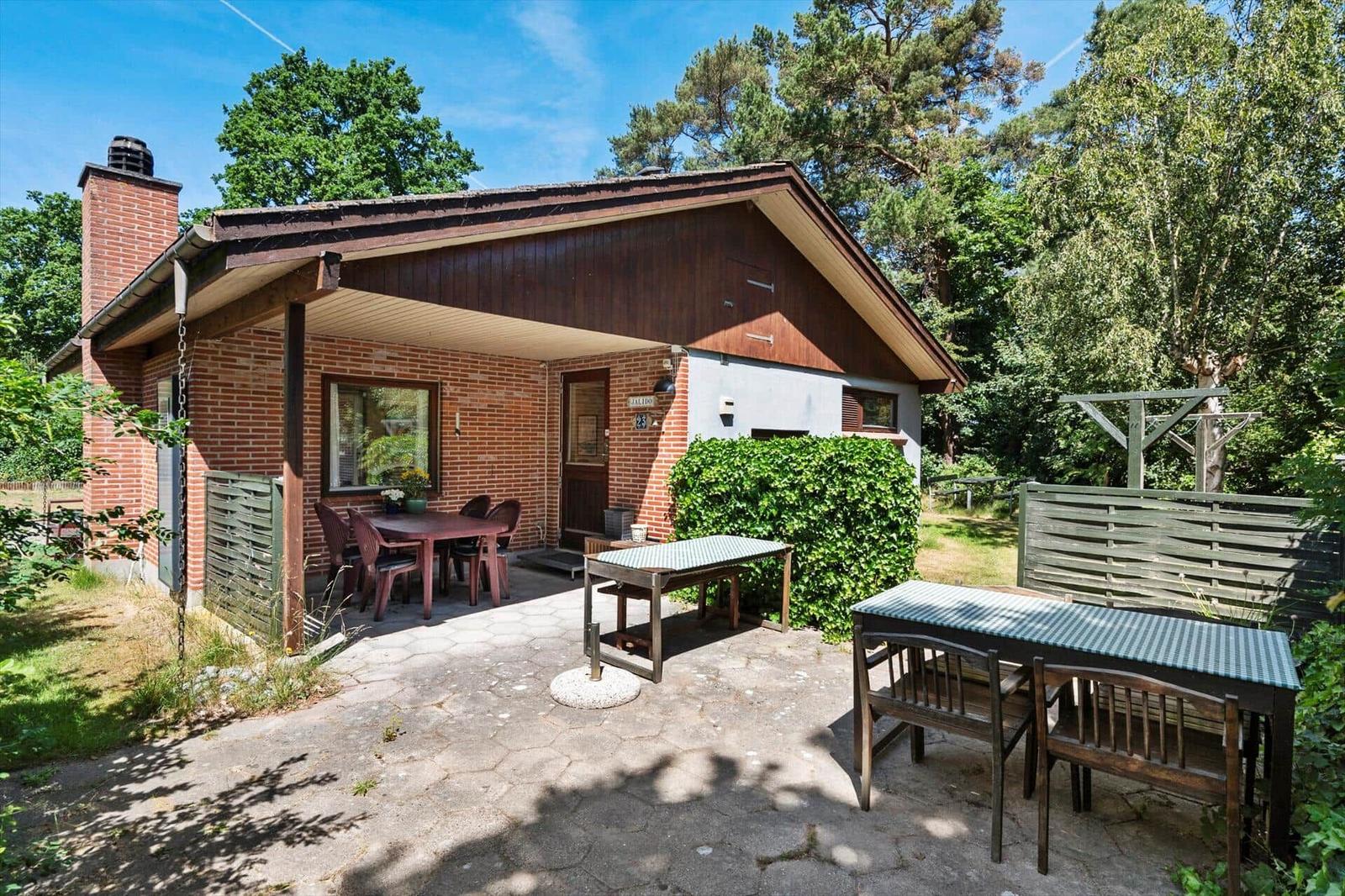 Haus mit Terrasse, Gartenmöbel und umgeben von Bäumen.