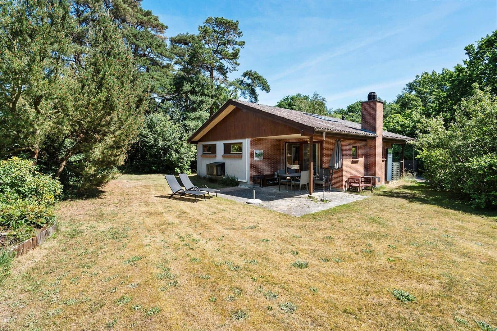 Haus mit Terrasse, Garten und Liegestühlen umgeben von Bäumen.