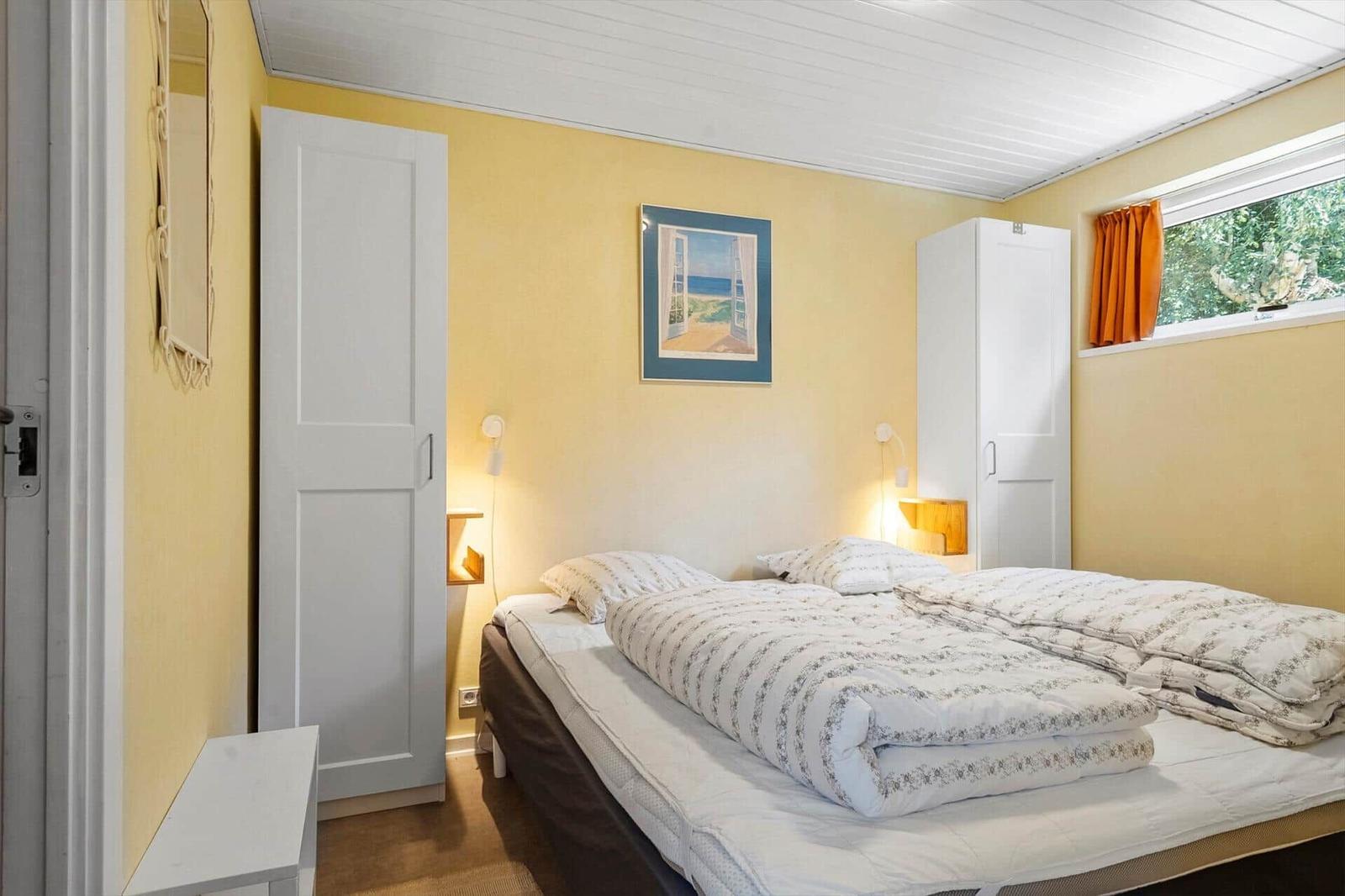 Schlafzimmer mit Bett, Kleiderschrank und Fenster mit orangefarbenen Vorhängen.