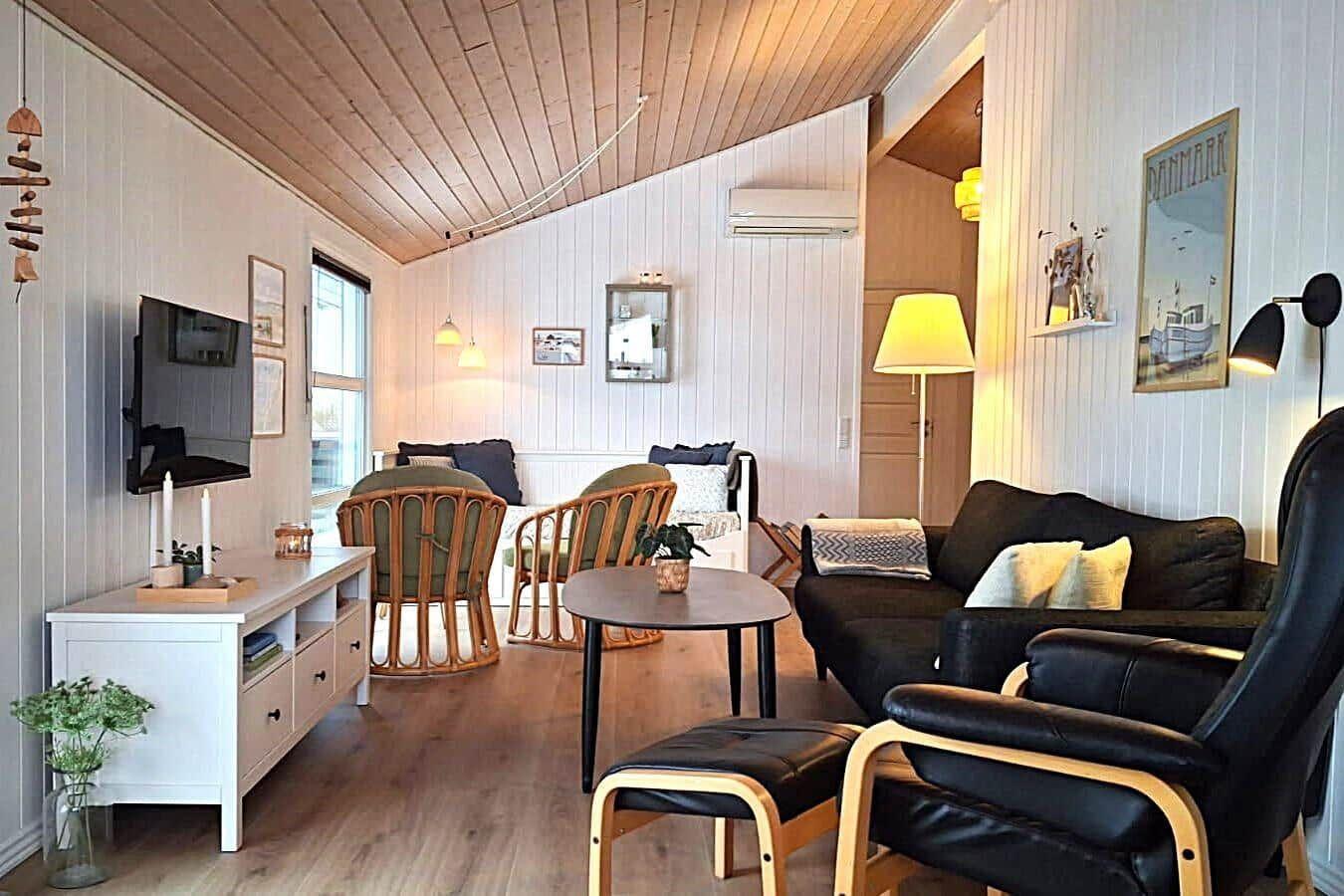 Wohnzimmer mit Sofa, Sesseln, Tisch und Fernseher an der Wand.
