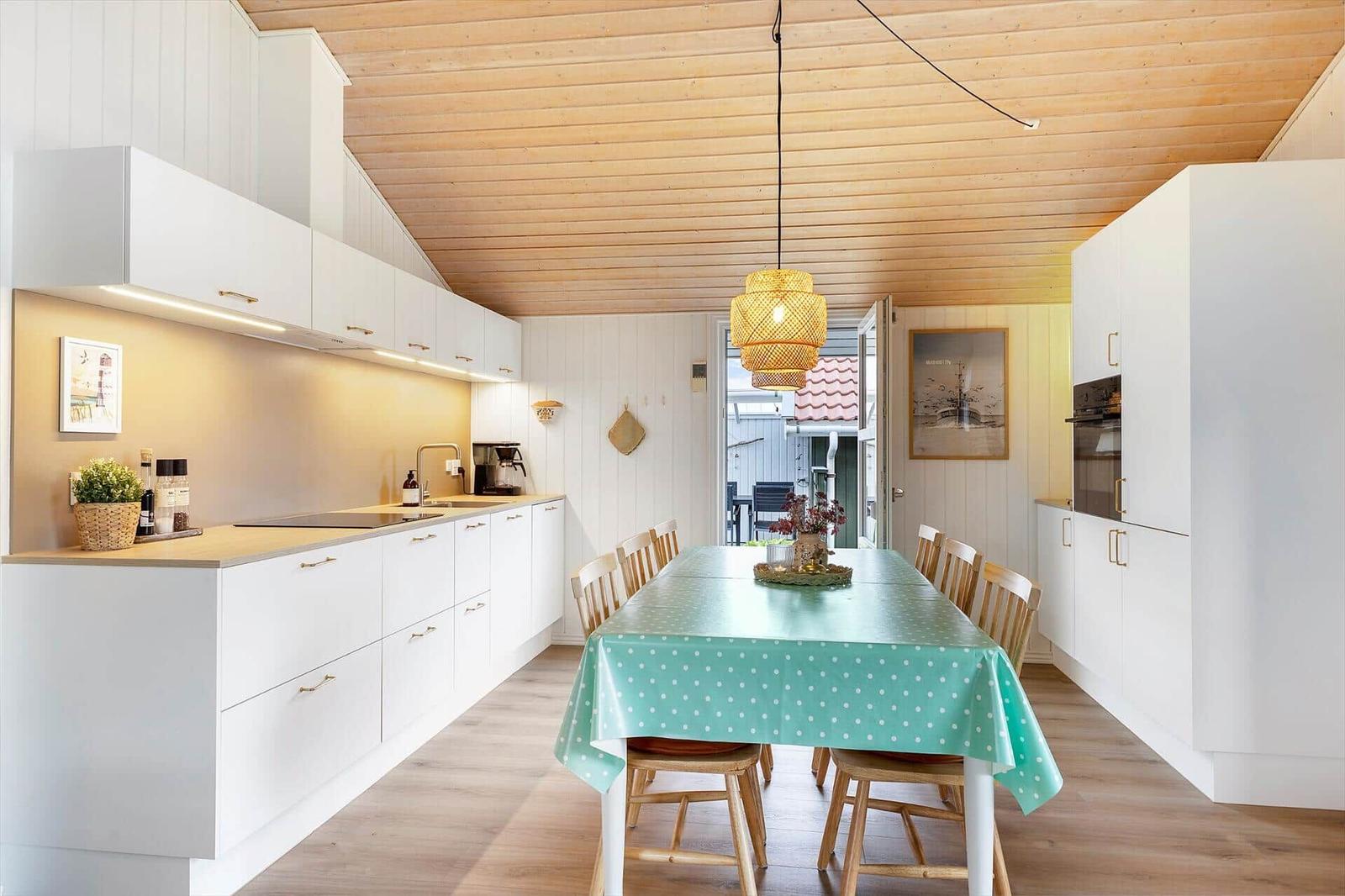 Küche mit Essbereich, weißer Einbauküche, Holzdecke und Tisch mit Tischdecke.