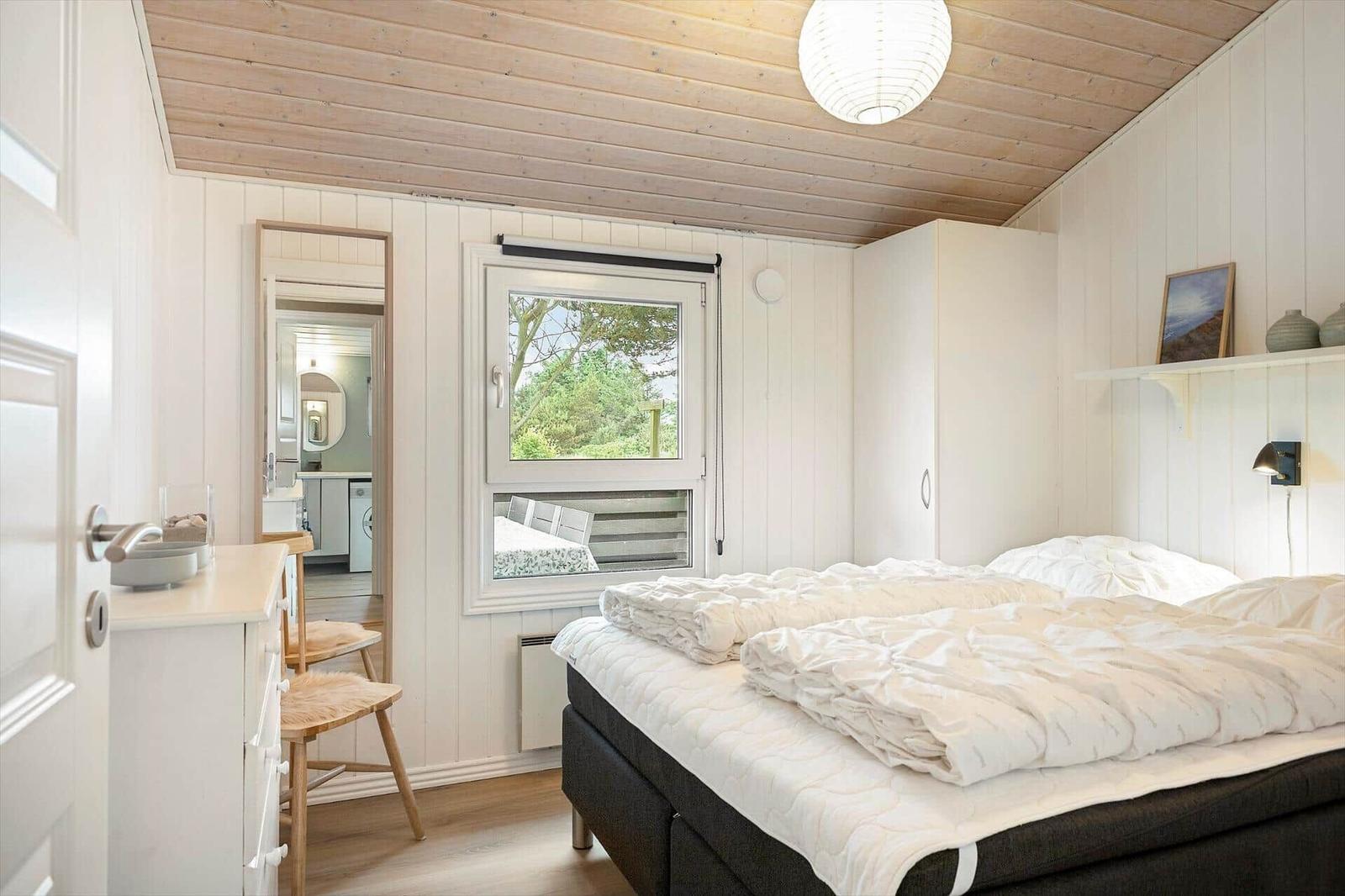Schlafzimmer mit Bett, Fenster und Waschbecken. Holzdecke und weiße Wände.