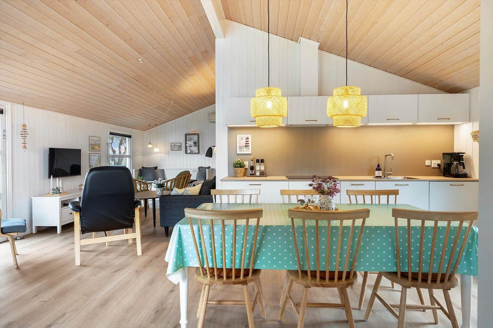 Esszimmer mit Holztisch, Stühlen und grünem Tischtuch. Küche und Wohnzimmer im Hintergrund.