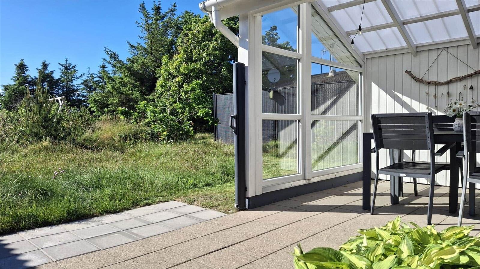 Terrasse mit Sitzgruppe, Glasfront und Blick auf grünen Garten.