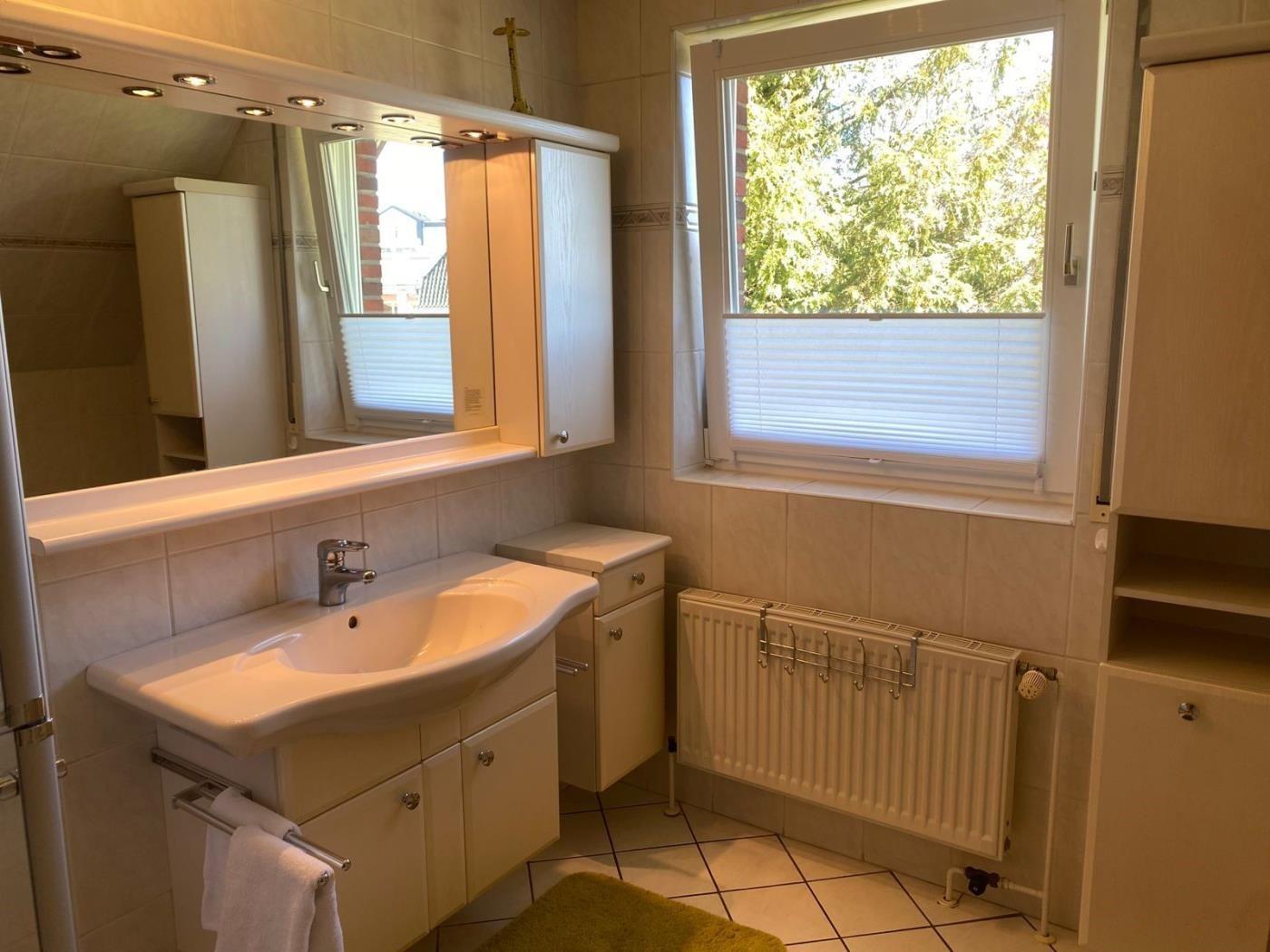 Badezimmer mit Waschbecken, Spiegelschrank und Fenster mit Jalousie.
