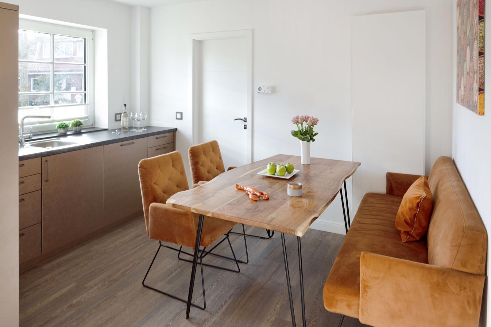 Essbereich mit Holztisch, braunen Sitzmöbeln und Küchenzeile im Hintergrund.