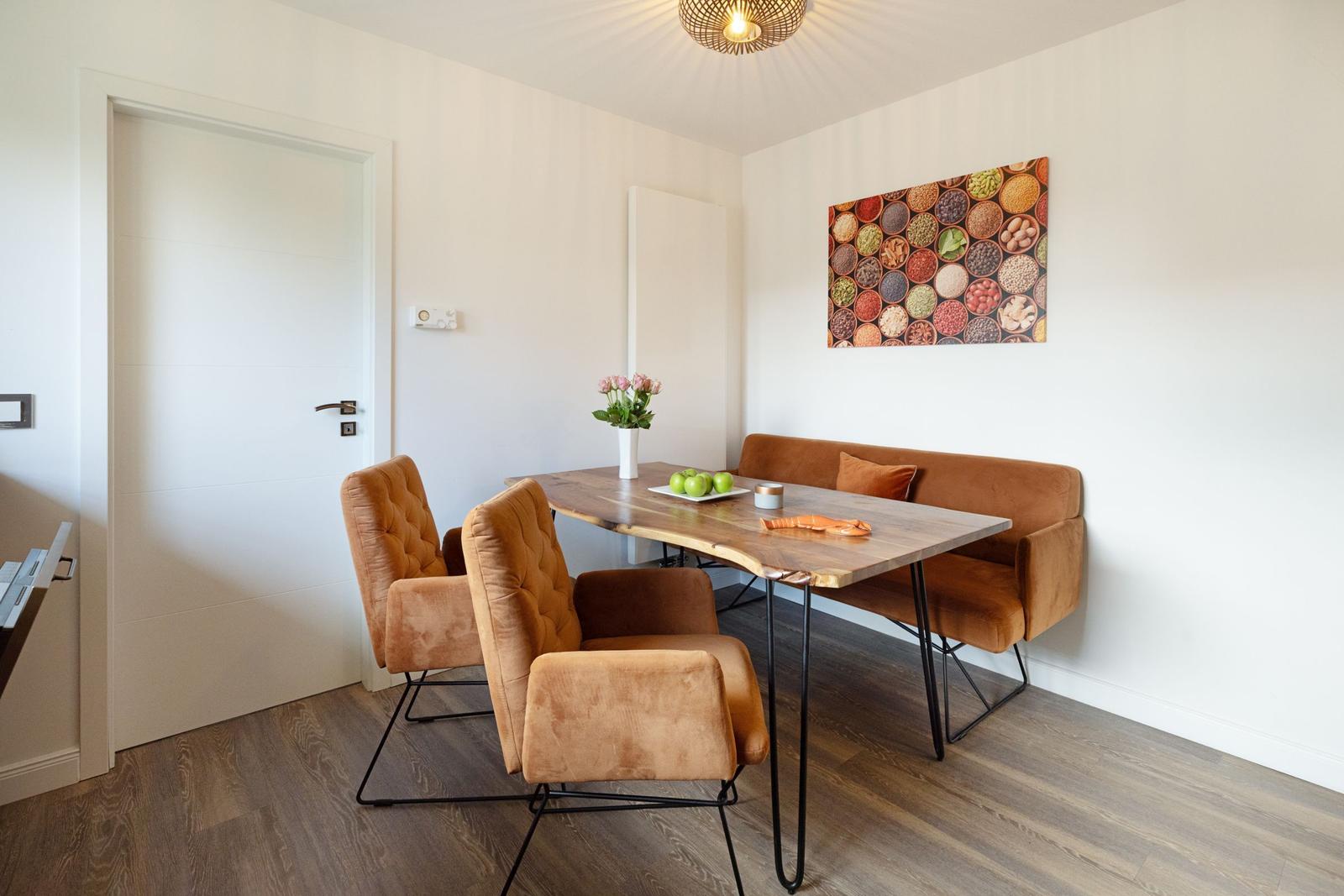 Essbereich mit Holztisch, braunen Sitzgelegenheiten und Wandbild mit Getreide.