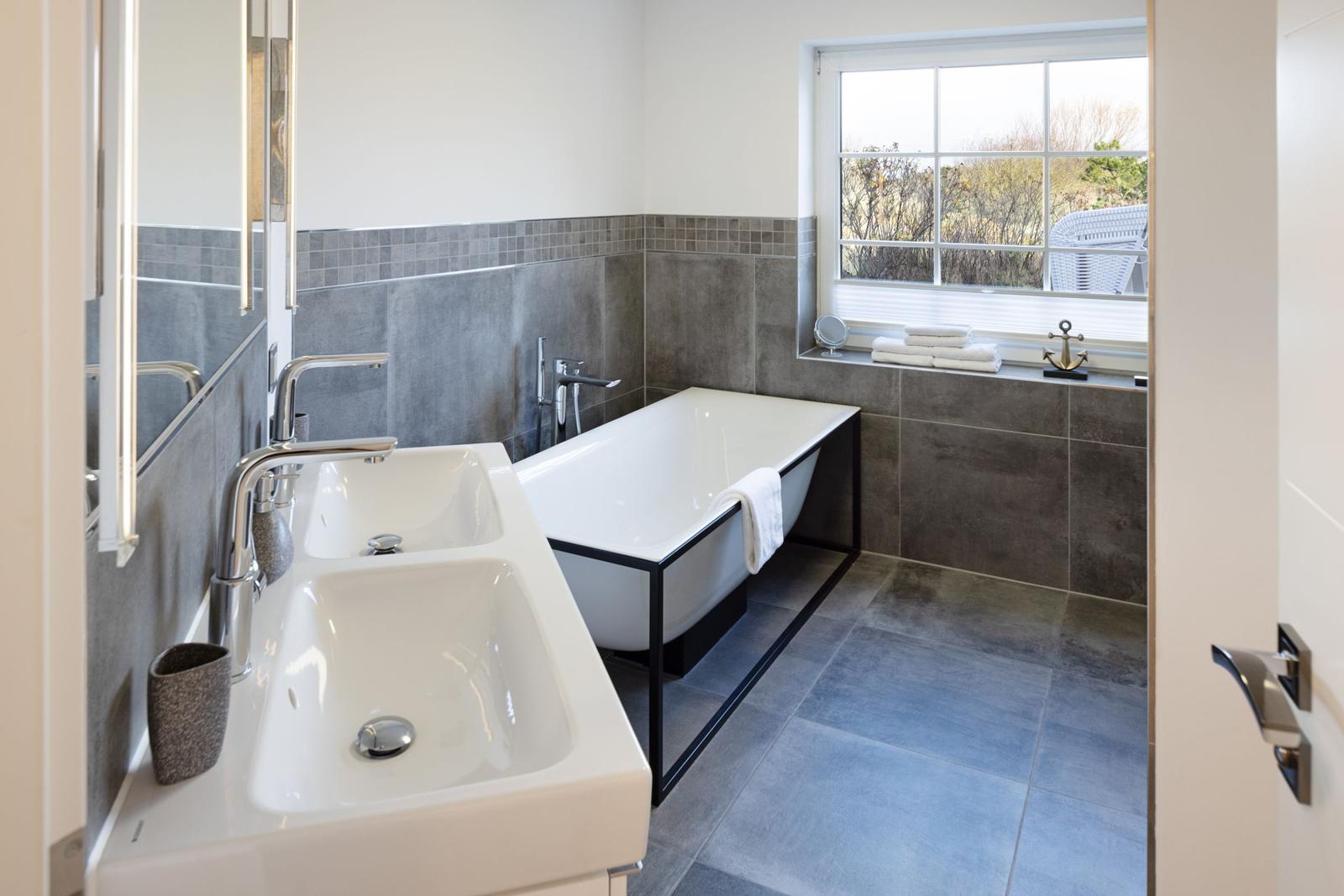 Badezimmer mit Badewanne, Waschbecken und Fenster mit Blick nach draußen.
