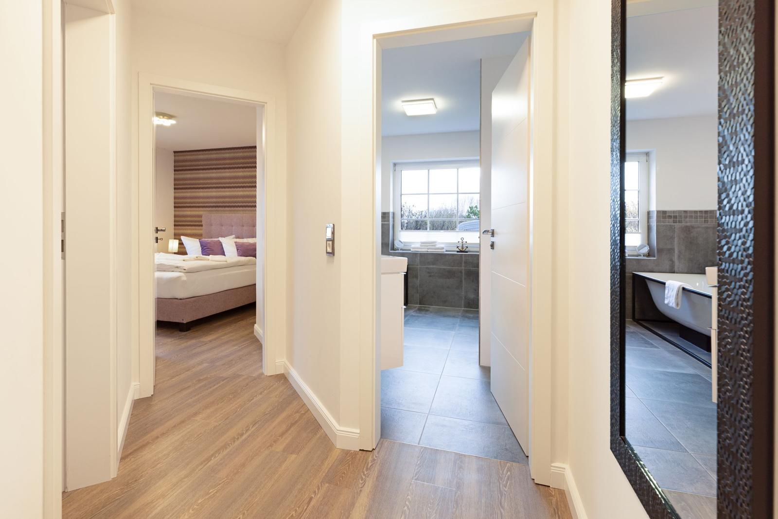 Flur mit Blick in Schlafzimmer und Bad mit Badewanne.