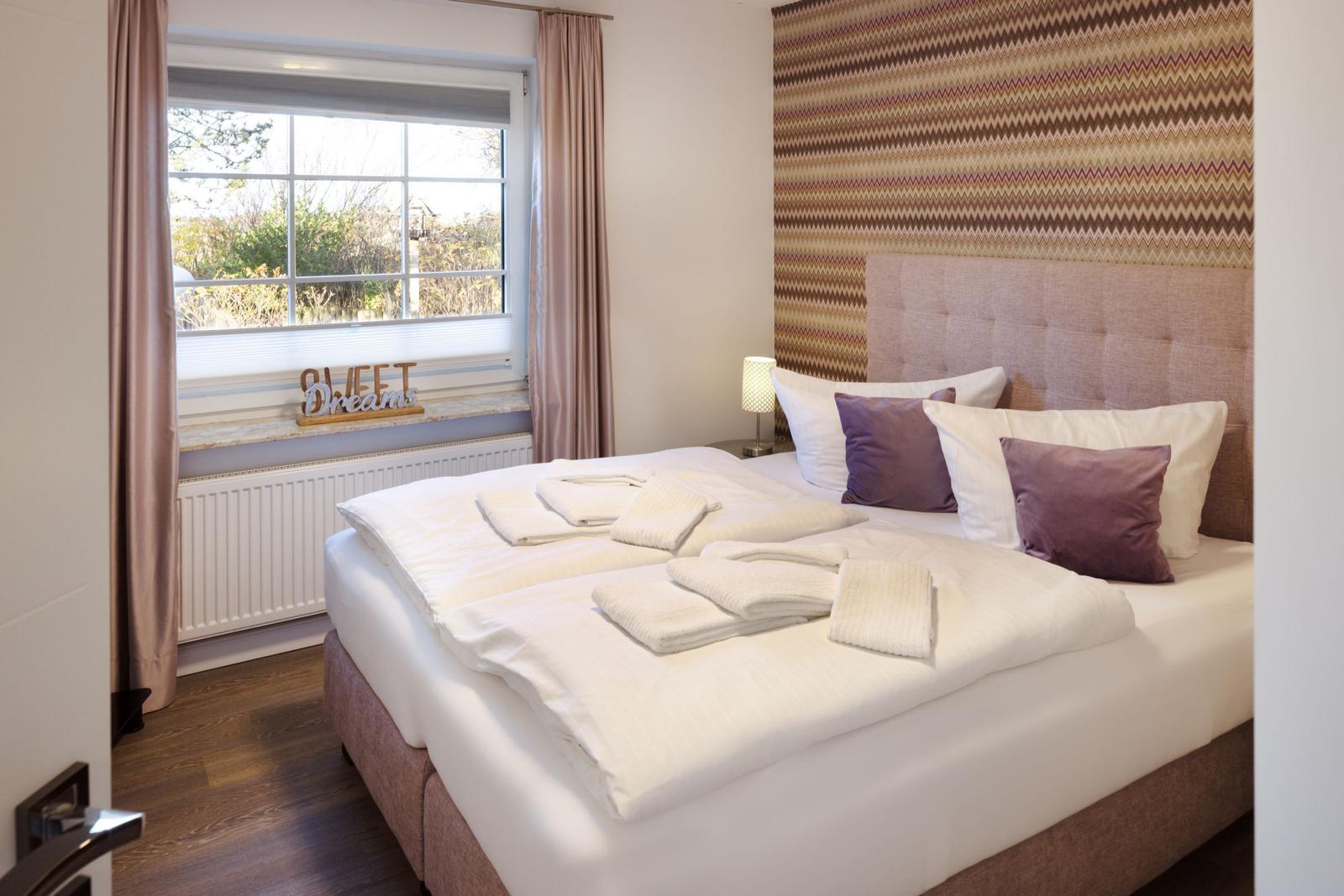 Schlafzimmer mit Bett, Fenster und gemusterter Wandverkleidung.