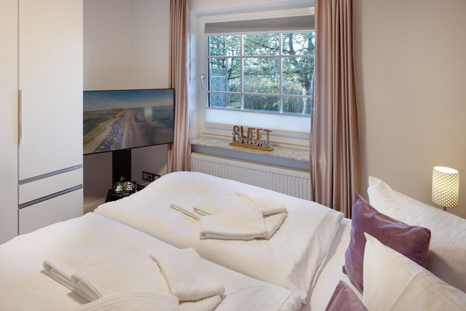 Schlafzimmer mit Doppelbett, TV und Fenster mit Blick auf Bäume.