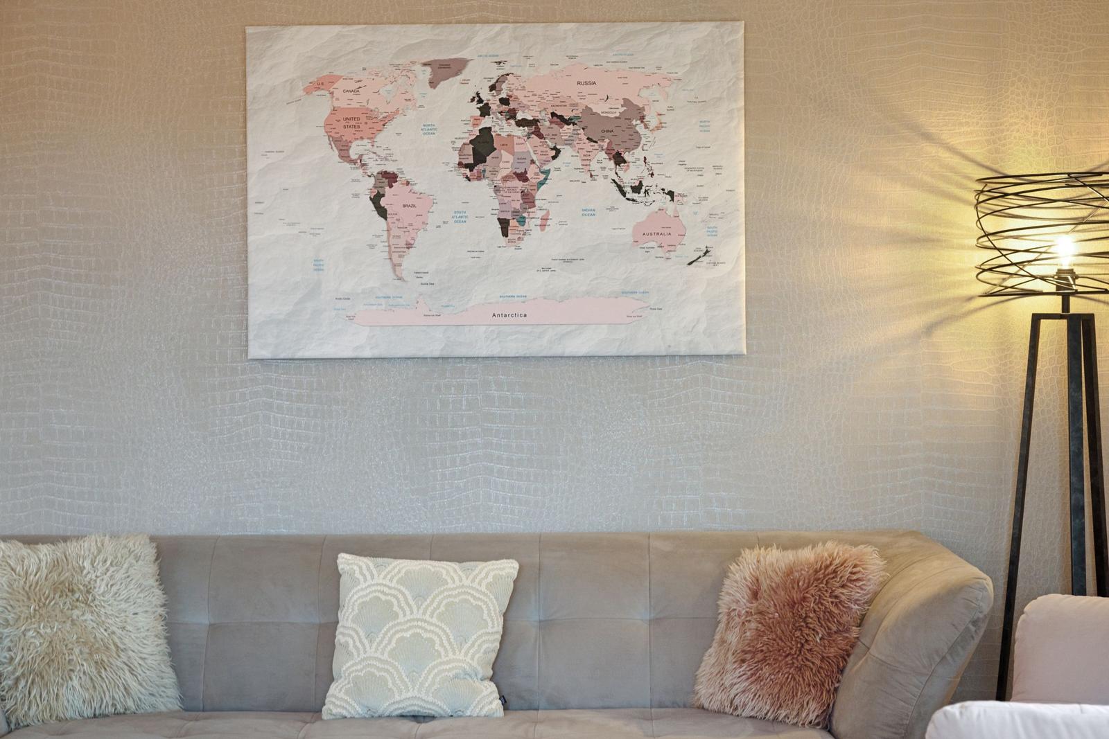 Ein Sofa mit Kissen unter einer Weltkarte an der Wand und einer Stehlampe rechts.