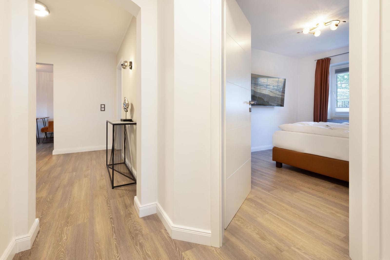 Schlafzimmer mit Bett und Fenster. Flur mit Tisch und Wandbeleuchtung.