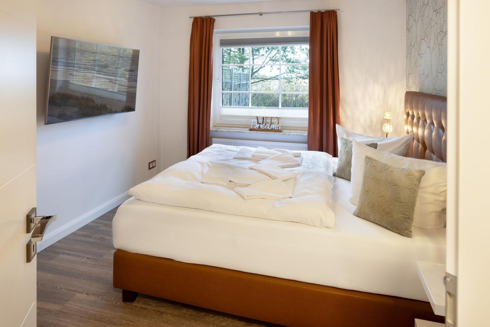 Schlafzimmer mit Bett, Fenster, TV und Vorhängen.