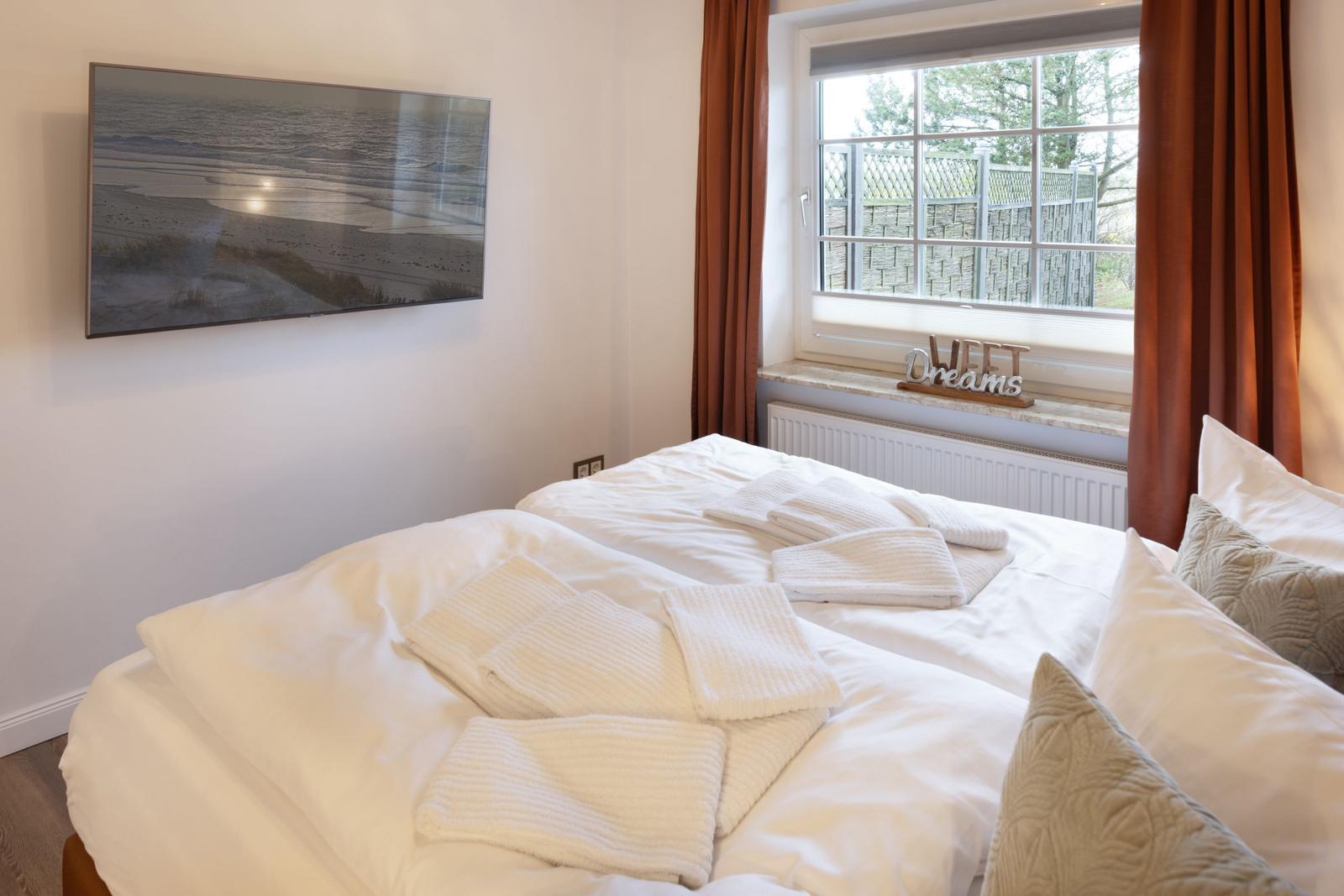 Schlafzimmer mit Bett, Fenster und Wandbild. Handtuch auf Bett. Vorhänge und Dekoration.