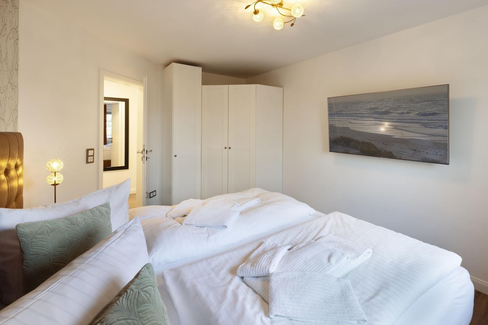 Schlafzimmer mit Bett, Kleiderschrank und Wandbild. Beleuchtung durch Deckenleuchte und Stehlampe.