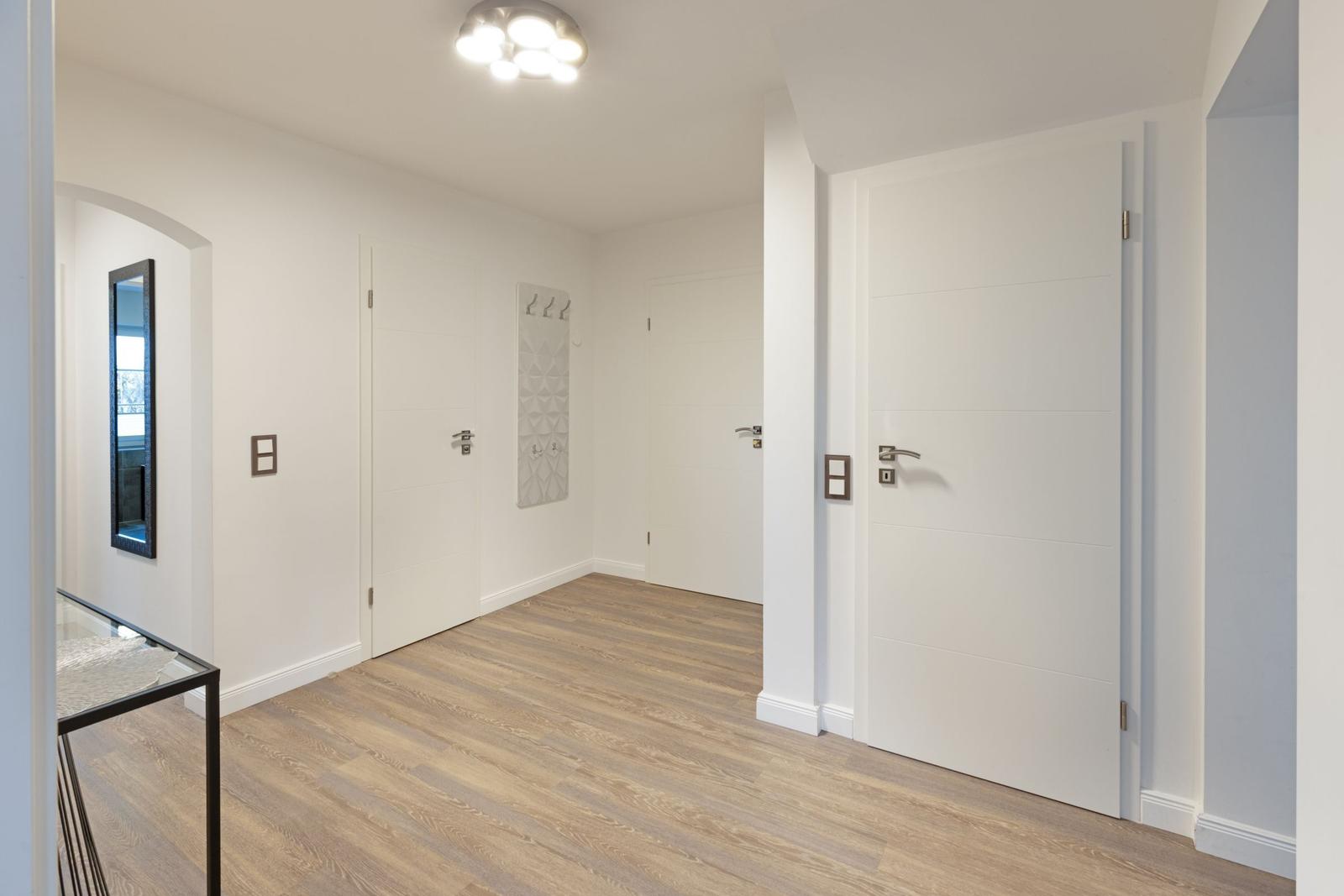 Helle Eingangshalle mit Holzboden und weißen Türen. Spiegel und Garderobe sind sichtbar.
