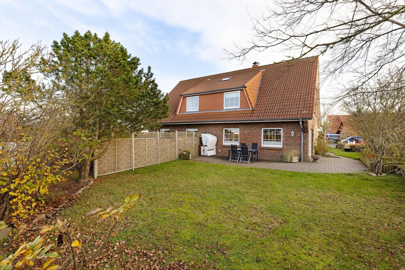 Ein Haus mit Garten, Terrasse und Grill. Umgeben von Bäumen und einem Zaun.