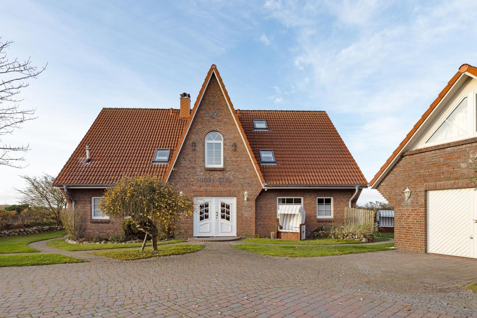 Rotes Ziegeldach, weiße Türen, gepflasterter Hof und Garten mit Bäumen.