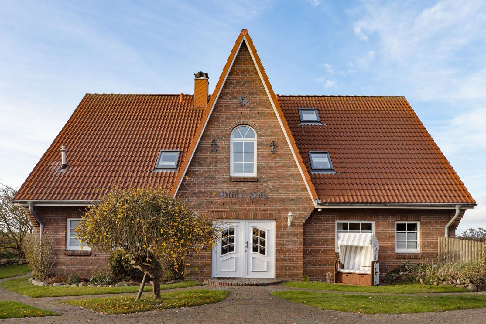 Haus mit rotem Ziegeldach, weißer Eingangstür und Gartenhaus.